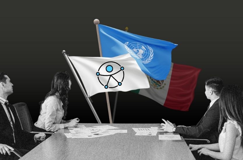 Personas en mesa de trabajo observan banderas de México y la ONU junto a un símbolo de discapacidad.